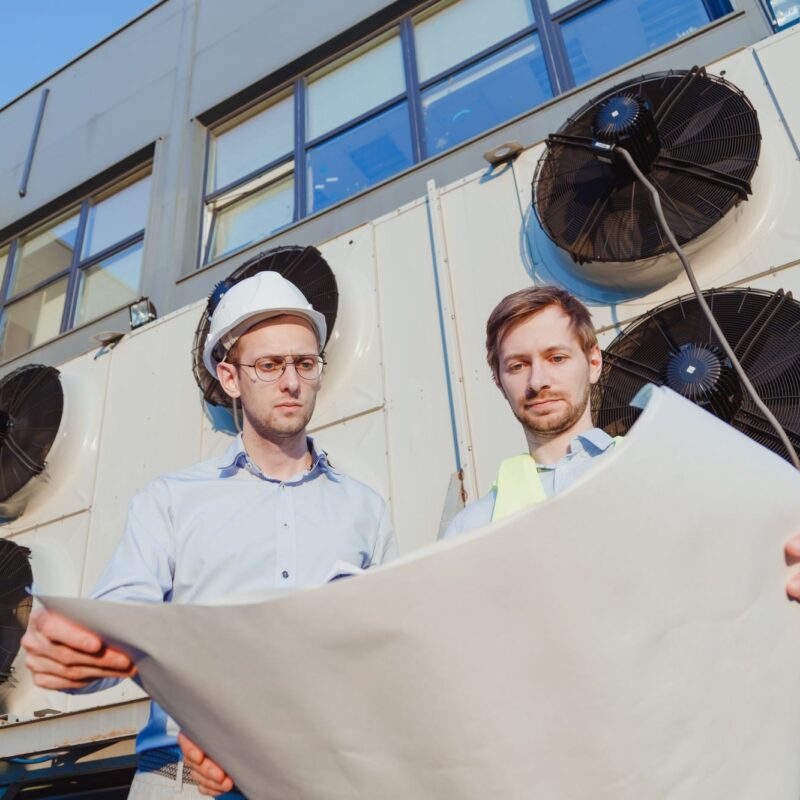 Service hvac engineer and internship in uniform with paper drawings at industrial fridge machine Service hvac engineer and internship in uniform with paper drawings at industrial fridge machine